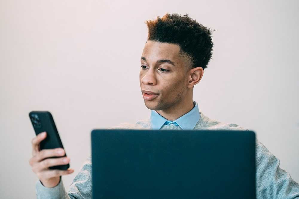 A man with a mobile phone working on a laptop